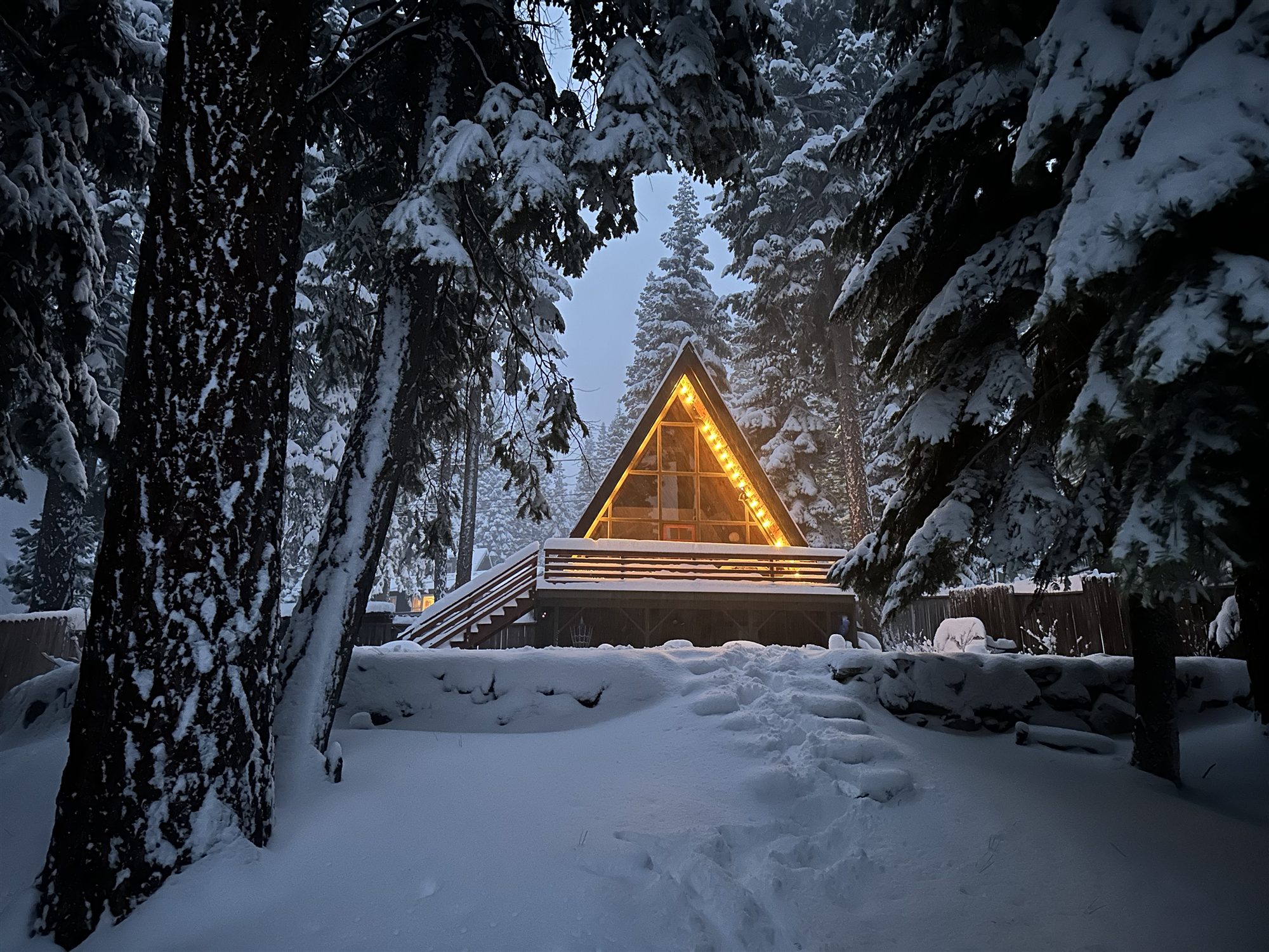 The deck glowing with string lights in fresh snow at dusk
