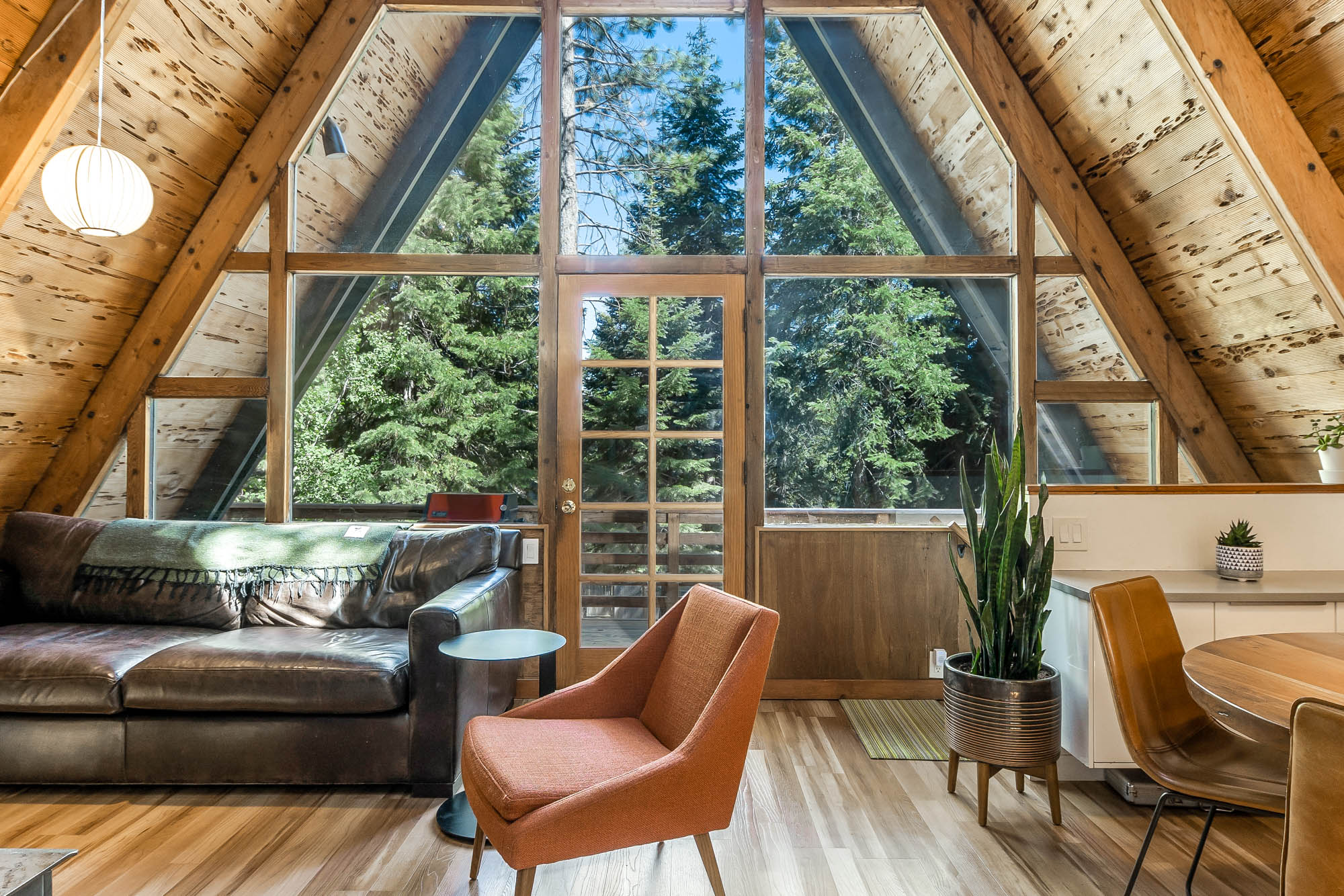 The great room — a double-height wall of glass facing the pines, leather sofa and mid-century chairs